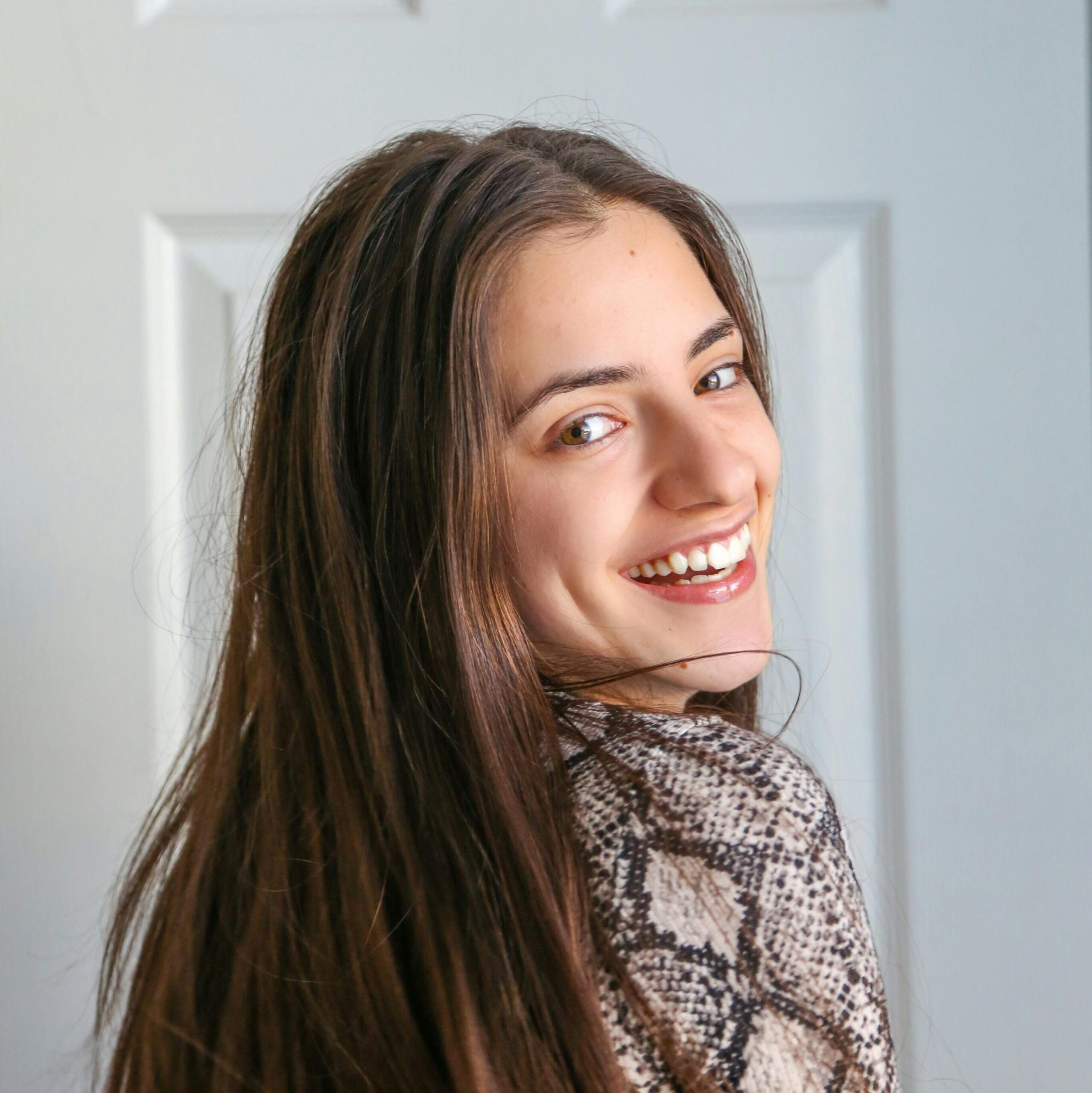 Cheerful young woman with long hair smiling indoors, exuding confidence and positivity.