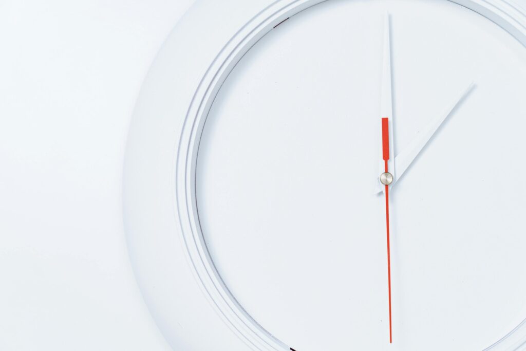 Close-up of a minimalist white wall clock with red hands, showcasing a sleek design.