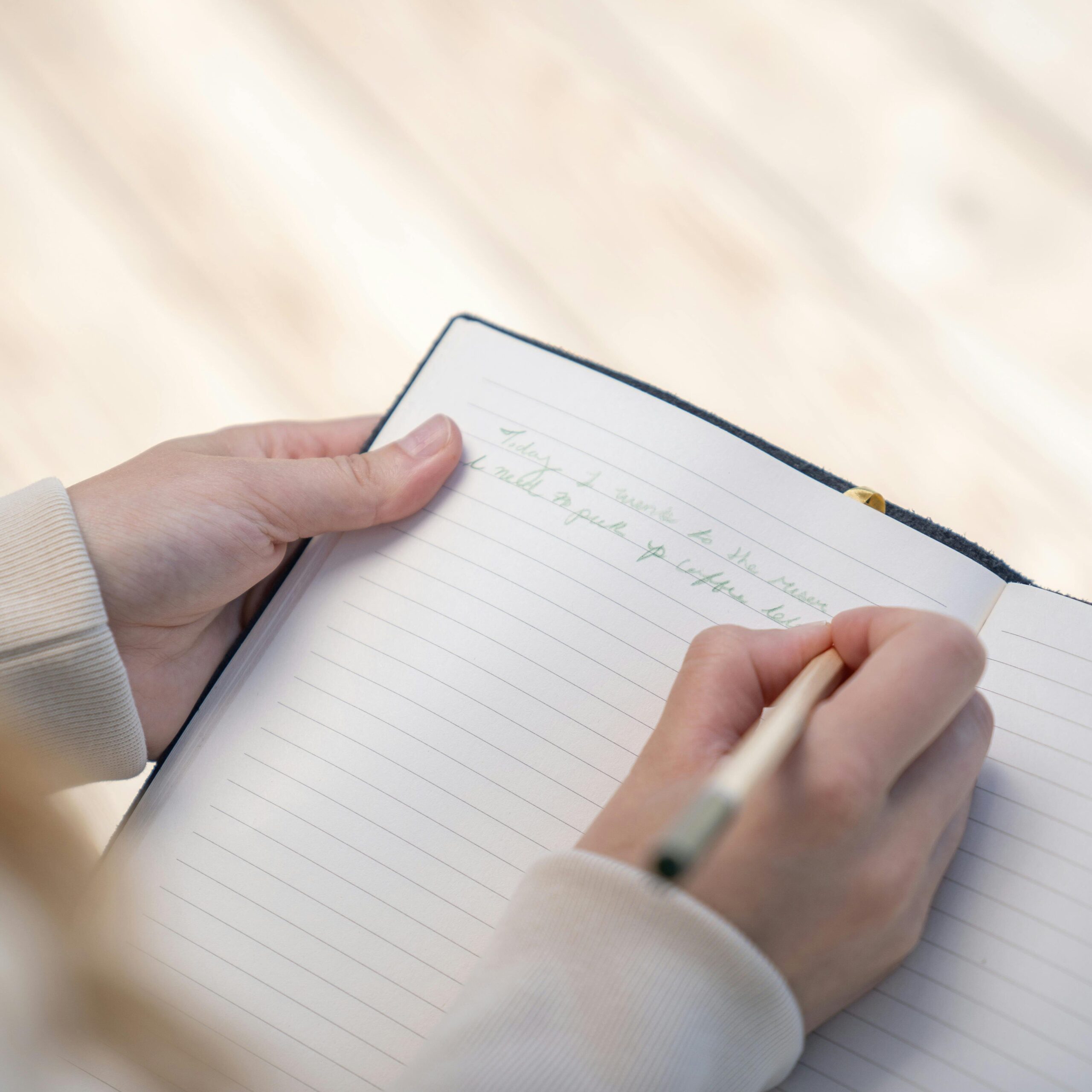 A person writing in a notebook with a pen, capturing a close-up view of hands.